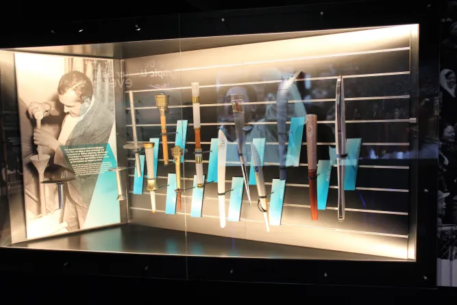 Beleuchtete Museums-Vitrine mit historischen Blasinstrumenten und Schildern; links ein Schwarzweißfoto eines Mannes..