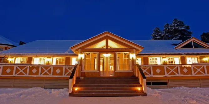Symmetrischer Eingangsbereich eines Hauses mit breiter Treppe, warmem Licht und schneebedecktem Dach bei Dämmerung..