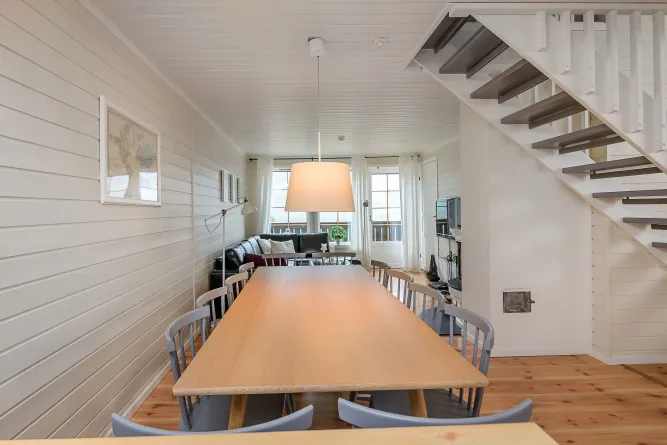 Heller Wohn-Essbereich mit langem Holztisch, Stühlen, großer Hängelampe und Treppe rechts neben dem Wohnzimmer..