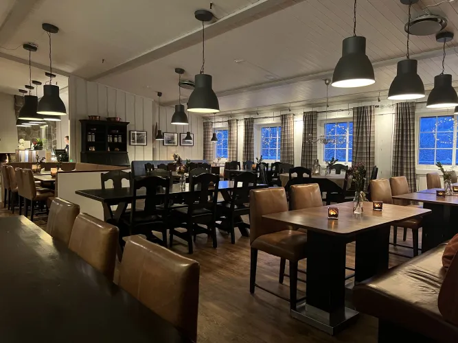 Leerer Restaurant-Gastraum mit Holztischen, Lederstühlen, Hängelampen und Fenstern mit Vorhängen bei Dämmerung..