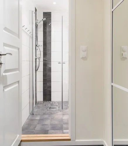 Lichte badkamer met inloopdouche, glazen douchewand, grijze tegelvloer en witte wandtegels met donkere strook..