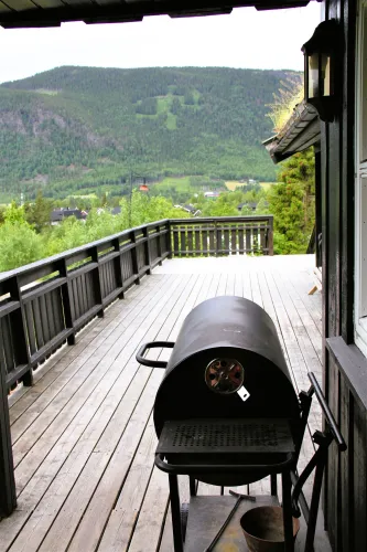 Houten veranda met zwarte barbecue op de voorgrond en uitzicht op een groen berglandschap en dorp in de verte..