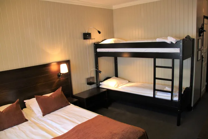 Gemütliches Hotelzimmer mit Doppelbett und schwarzem Etagenbett, Nachtlampen an der Wand und neutralen Holzwänden..