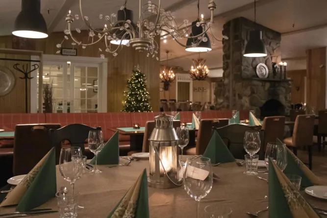 Gedeckter Restauranttisch mit Laterne, Gläsern und Servietten; im Hintergrund Kronleuchter, Kamin und Weihnachtsbaum..