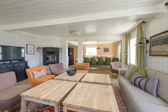 Helles, gemütliches Wohnzimmer mit Sofa, Sesseln, Couchtischen, Kamin, TV und Essbereich mit grünen Stühlen..