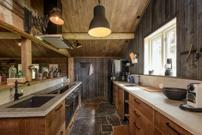 Rustikale Küche mit Holzdecke, Hängelampen, Stein-Arbeitsplatten, Spüle, Herd, Kühlschrank und Fensterlicht..