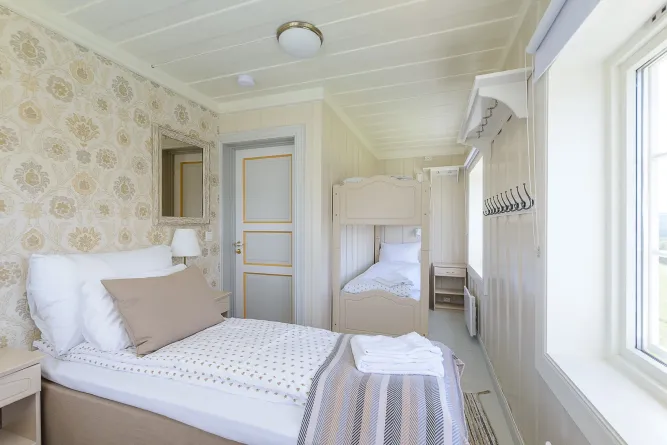 Helles Schlafzimmer mit Doppelbett im Vordergrund, Etagenbett hinten, kleinem Nachttisch und großem Fenster rechts..