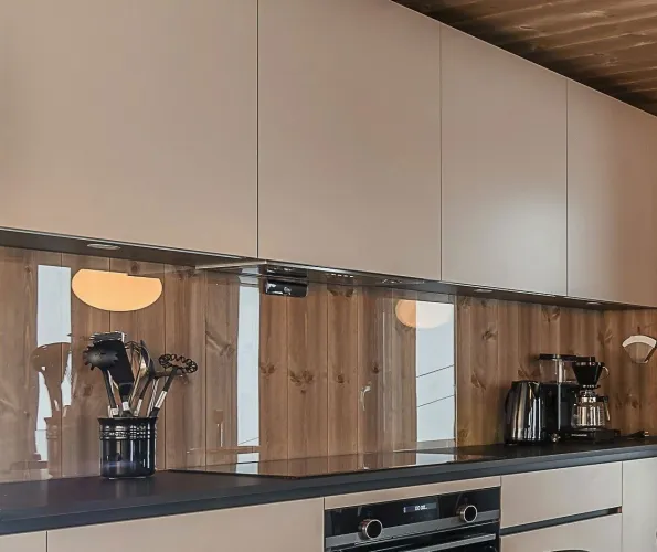 Moderne Küchenzeile mit hellen Hängeschränken, Holzrückwand, dunkler Arbeitsplatte sowie Küchenutensilien und Kaffeemaschine..