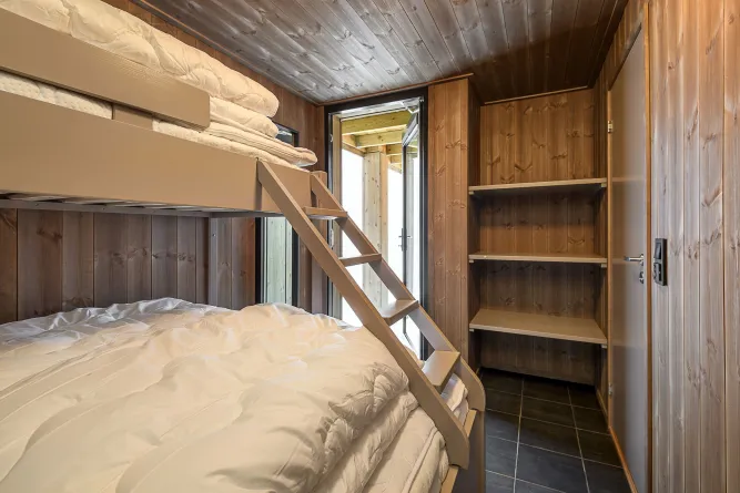 Kleines Schlafzimmer mit Holzvertäfelung, Etagenbett und Leiter, weißen Bettdecken, Regal und offener Glastür..