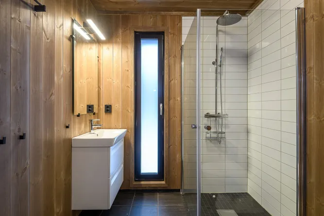 Helles Badezimmer mit Holzvertäfelung, Waschtisch mit Spiegel und begehbarer Dusche mit Glaswand und Regenduschkopf..