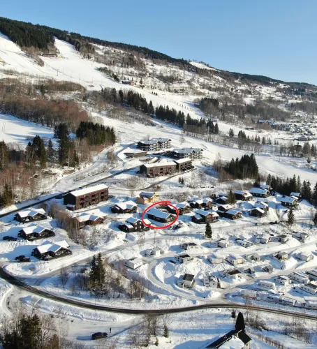 Luchtfoto van een besneeuwd bergdorp met chalets, wegen en bomen onder een heldere blauwe lucht..