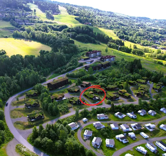 Luchtfoto van een groen vakantiepark met huisjes, kronkelwegen en caravans, met een rood omcirkeld huisje..