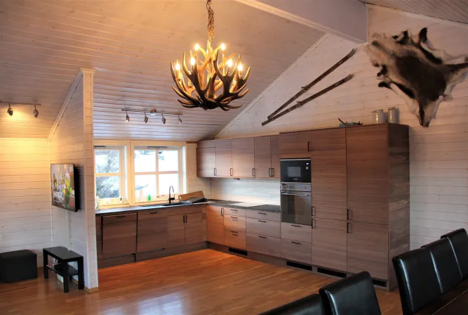 Houten keuken in chaletstijl met gewei-kroonluchter, donkere kasten, raam bij spoelbak en ski’s aan de wand..