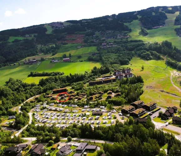 Luchtfoto van een groen bergdal met bos, velden, chaletpark en camping met caravans langs kronkelwegen..