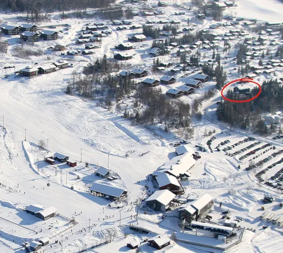 Luchtfoto van een besneeuwd skigebied met pistes, liftgebouwen, chalets en parkeerplaats; rode cirkel rechts..