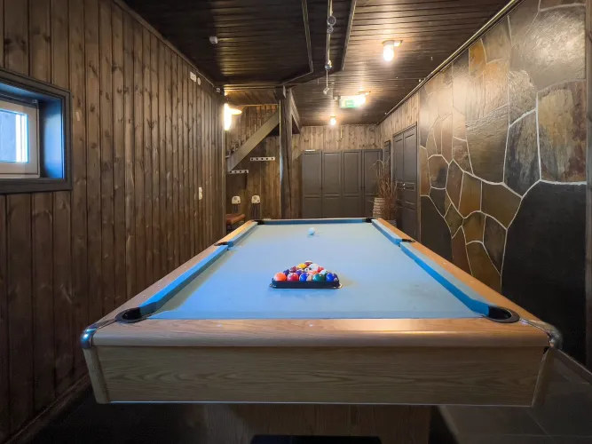 Binnenruimte met een biljarttafel met blauwe stof en gekleurde ballen, omgeven door houten wanden en lampen..