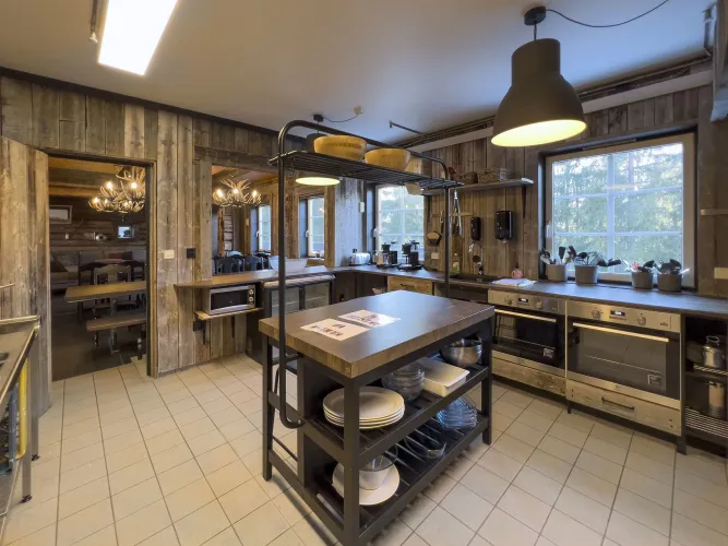 Rustieke houten keuken met kookeiland, hanglampen, ovens en een groot raam met uitzicht op bomen..