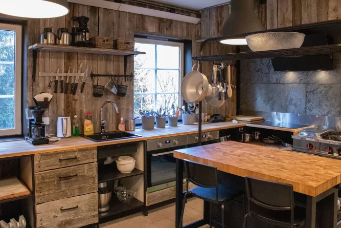 Gezellige rustieke keuken met houten kasten, kookeiland, hangende pannen, gootsteen en ramen met sneeuw buiten..