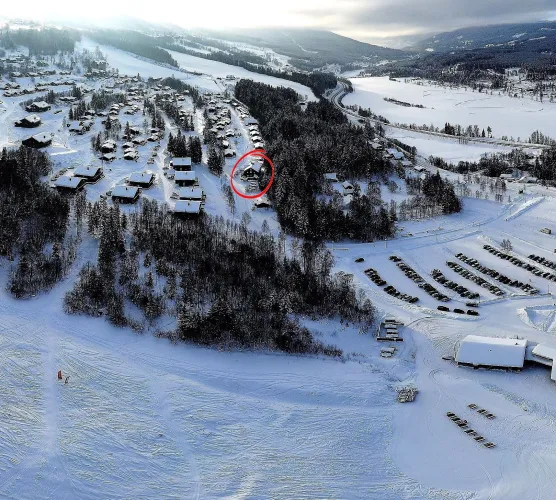 Luchtfoto van een besneeuwd bergdorp met chalets, bosrand en parkeerterrein; een huis is rood omcirkeld..