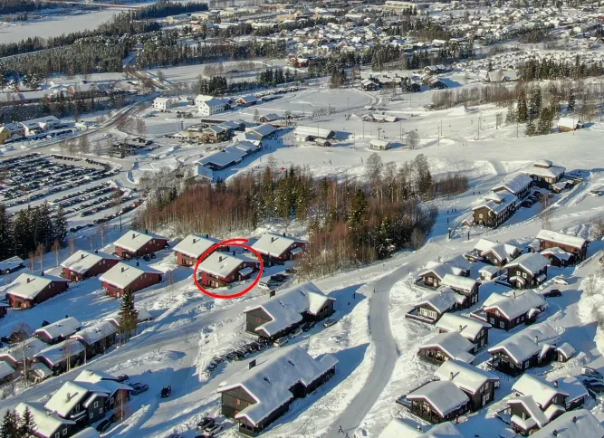 Luftaufnahme einer verschneiten Wohnsiedlung mit roten Häusern, Straßen und Waldstreifen; ein Haus ist rot markiert..