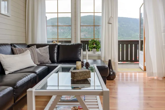 Modernes Wohnzimmer mit schwarzem Ledersofa, Glastisch und großen Fenstern mit Blick auf Berge und Balkon..