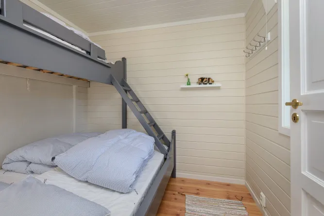 Helles Schlafzimmer mit grauem Etagenbett, Leiter, Bettwäsche, Holzfußboden, kleiner Wandablage und Tür..