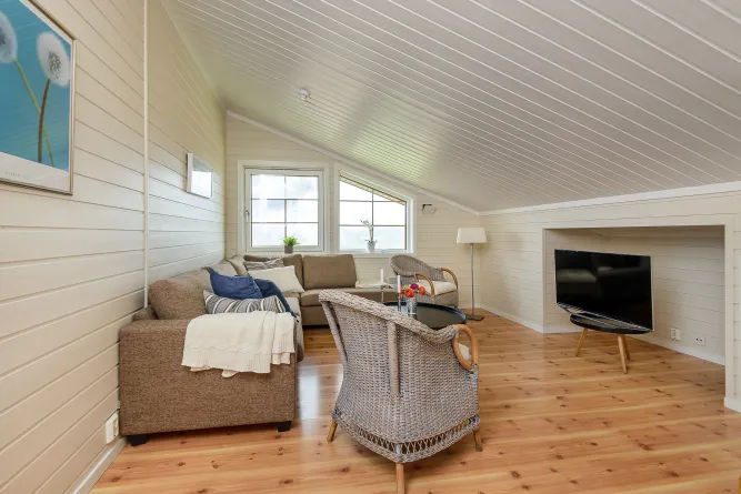 Gemütliches Wohnzimmer unterm Dach mit Sofa, Korbsesseln, Couchtisch, Stehlampe und Fernseher auf Holzboden..