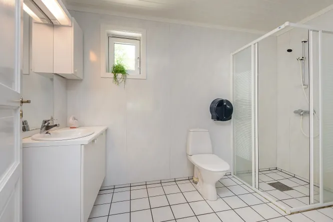 Modernes weißes Badezimmer mit Waschtisch links, WC mittig, Duschkabine rechts und kleinem Fenster mit Pflanze..