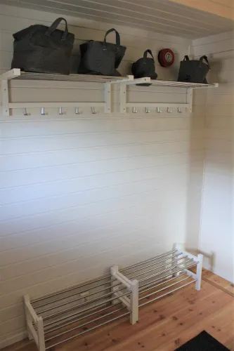 Weiße Holzpaneelwand mit Garderobenhaken, zwei Ablagen mit Taschen, Schuhregal aus Metall und Holzfußboden..