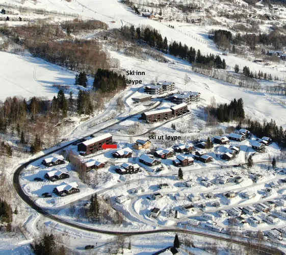 Luftaufnahme eines verschneiten Dorfes mit Hütten, Straßen, Waldstücken und Skipisten in hügeliger Landschaft..