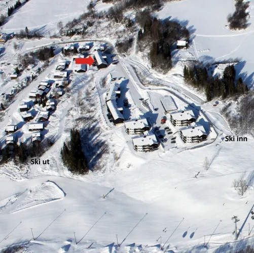 Luftaufnahme eines verschneiten Skigebiets mit Hotelanlagen, Häusern, Pistenflächen und Baumgruppen im Winter..
