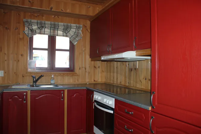 Holzvertäfelte Küche mit roten Schrankfronten, Spüle am Fenster, Herd und Backofen sowie Dunstabzugshaube..