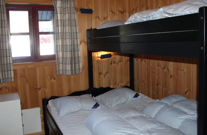 Kleines Schlafzimmer mit Holzvertäfelung, schwarzem Etagenbett, weißen Bettdecken und Fenster mit Vorhängen..