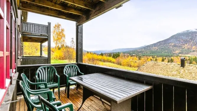 Überdachter Holz-Balkon mit Tisch und grünen Plastikstühlen, Blick auf herbstliche Bäume, Tal und Berge..