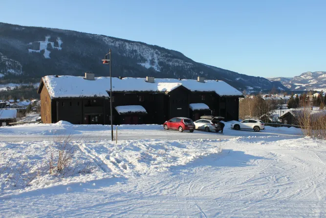 Schneebedeckte Lodge mit parkenden Autos vor einem Bergpanorama, klarer blauer Himmel und Wintersonne..