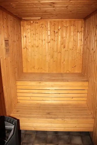 Lege sauna met houten wanden, plafond en zitbank, tegelvloer en een kachelhoek links onder in beeld..