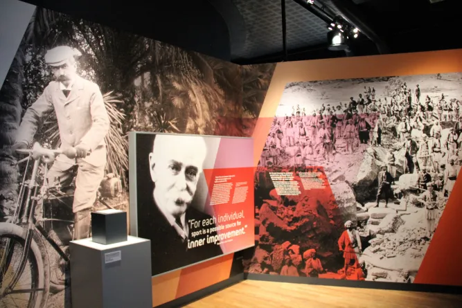 Ausstellungsraum mit großformatigen historischen Schwarzweißfotos, Texttafeln und einem Podest unter Deckenlicht..