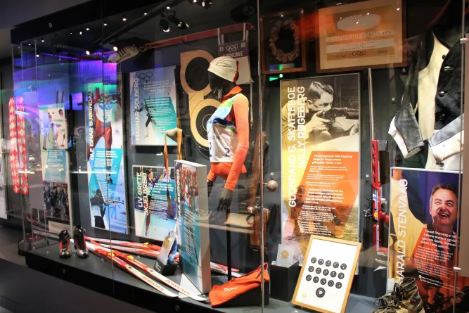 Museumsvitrine mit Ski, Skistöcken, Schuhen, Sportanzug und Infotafeln über Wintersportler unter Glas..