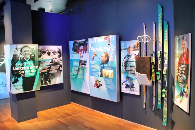 Innenansicht einer Ausstellung mit Infotafeln zu Paralympics und an der Wand montierten Skiern und Stöcken..