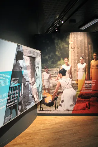 Innenraum einer Ausstellung mit großen Fototafeln, Holzfußboden und Deckenbeleuchtung; Personen auf Bildern zu sehen..