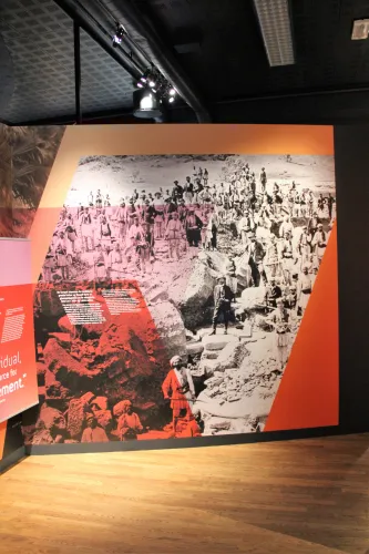 Innenraum einer Ausstellung mit großem Wandbild: historische Schwarzweiß-Fotografie einer Menschenmenge, rot überlagert..