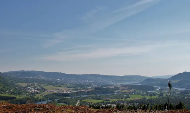 Panoramablick über ein grünes Tal mit Fluss, Feldern und Ortschaften, dahinter sanfte Hügel unter blauem Himmel..