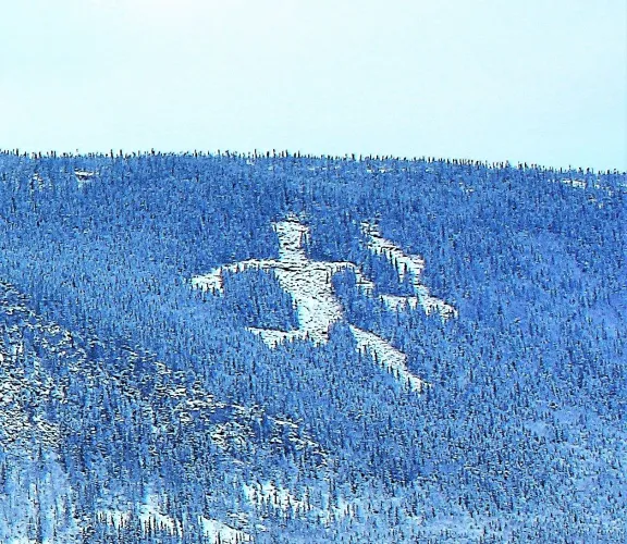 Besneeuwde open plek in een dicht naaldbos op een berghelling, met de vorm van een grote menselijke figuur..